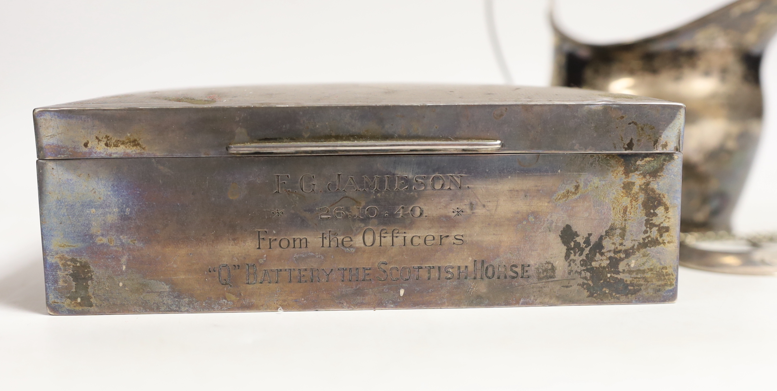A George V Art Deco silver mounted rectangular cigarette box, with engraved inscription, Birmingham, 1932, 15.1cm, a Georgian silver cream jug, maker possibly William Welch II of Exeter? and a Georgian silver crescent 'G